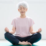 Older woman sitting with her legs crossed with her hands resting on her knees. 