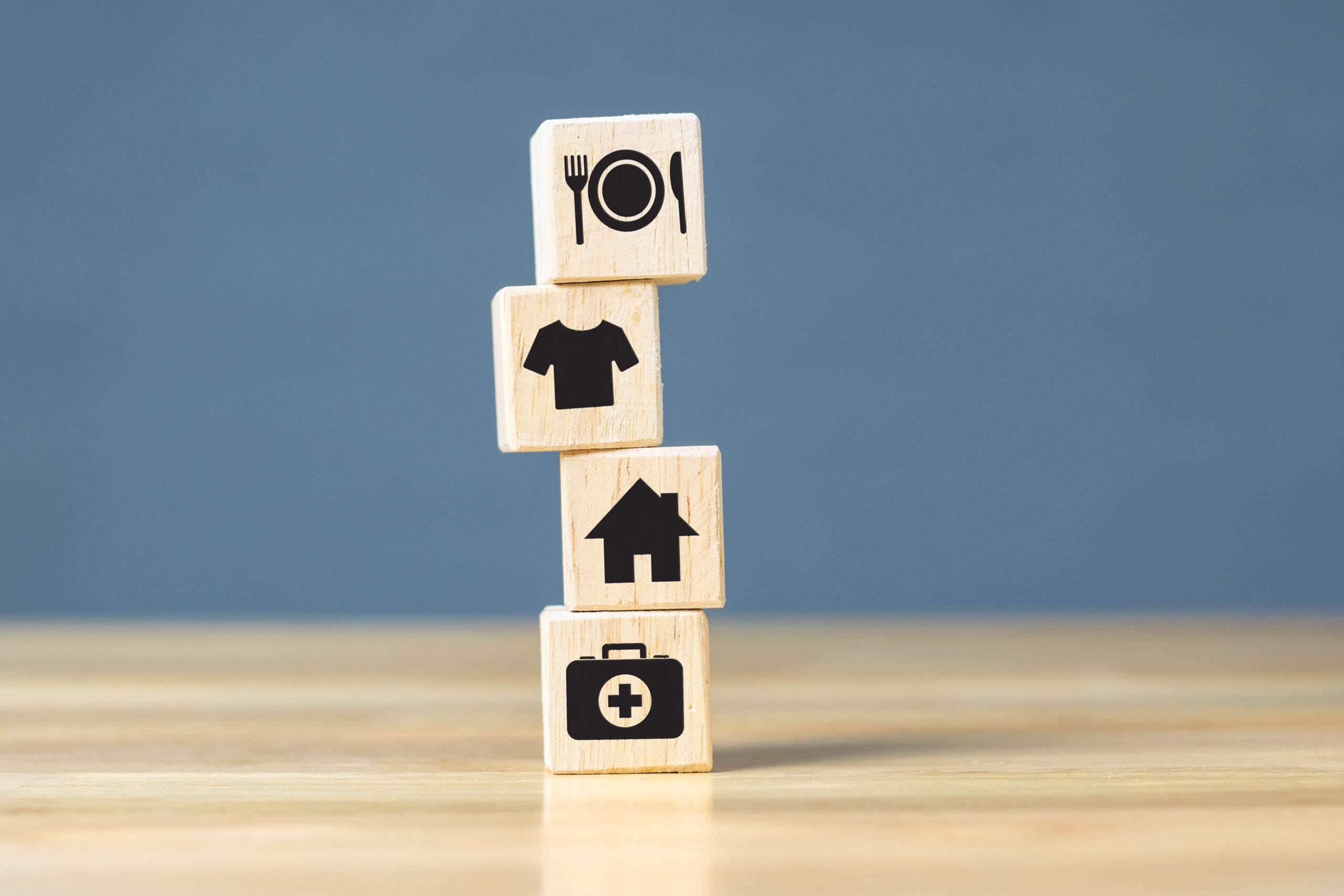 Stacked wooden cube blocks with icons for food, clothing, housing, and health care