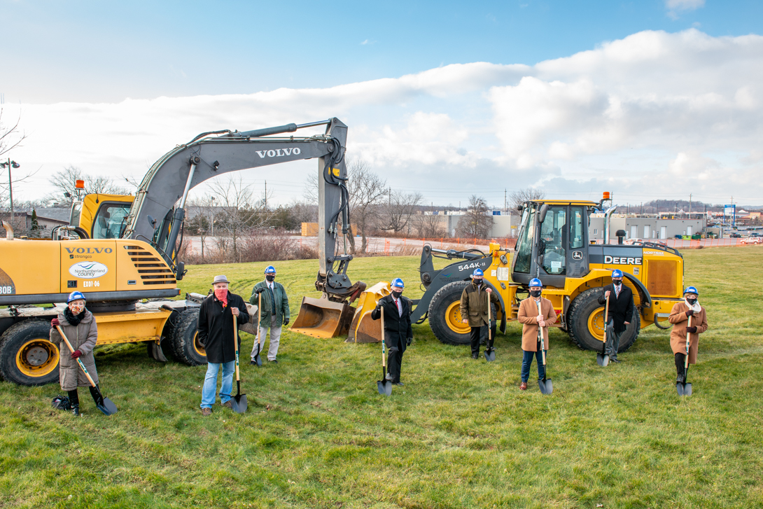 Council members holding shovels with large construction equipment behind them at the site of the new Golden Plough Lodge.