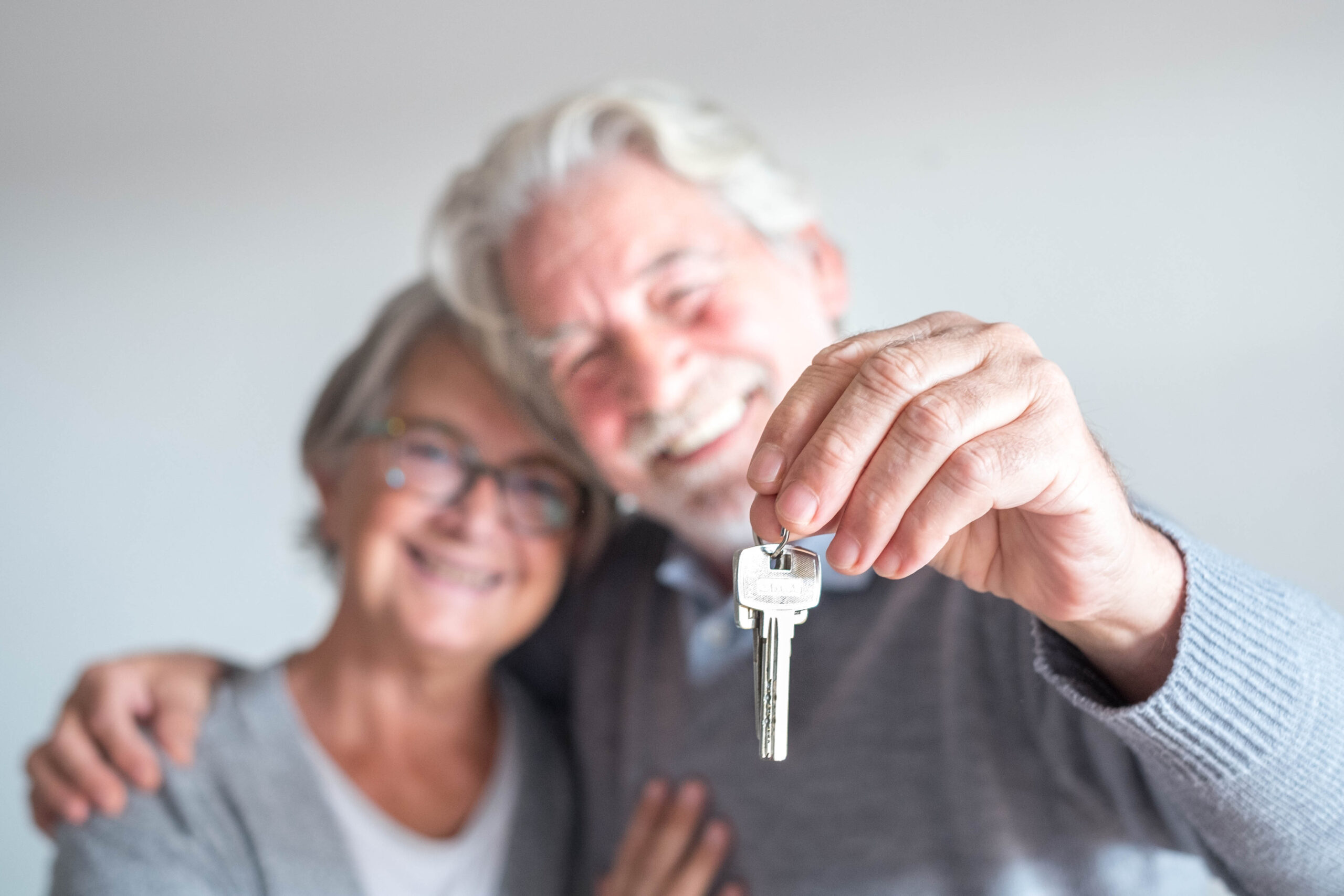 Senior couple hugs and holds house keys out in front of them