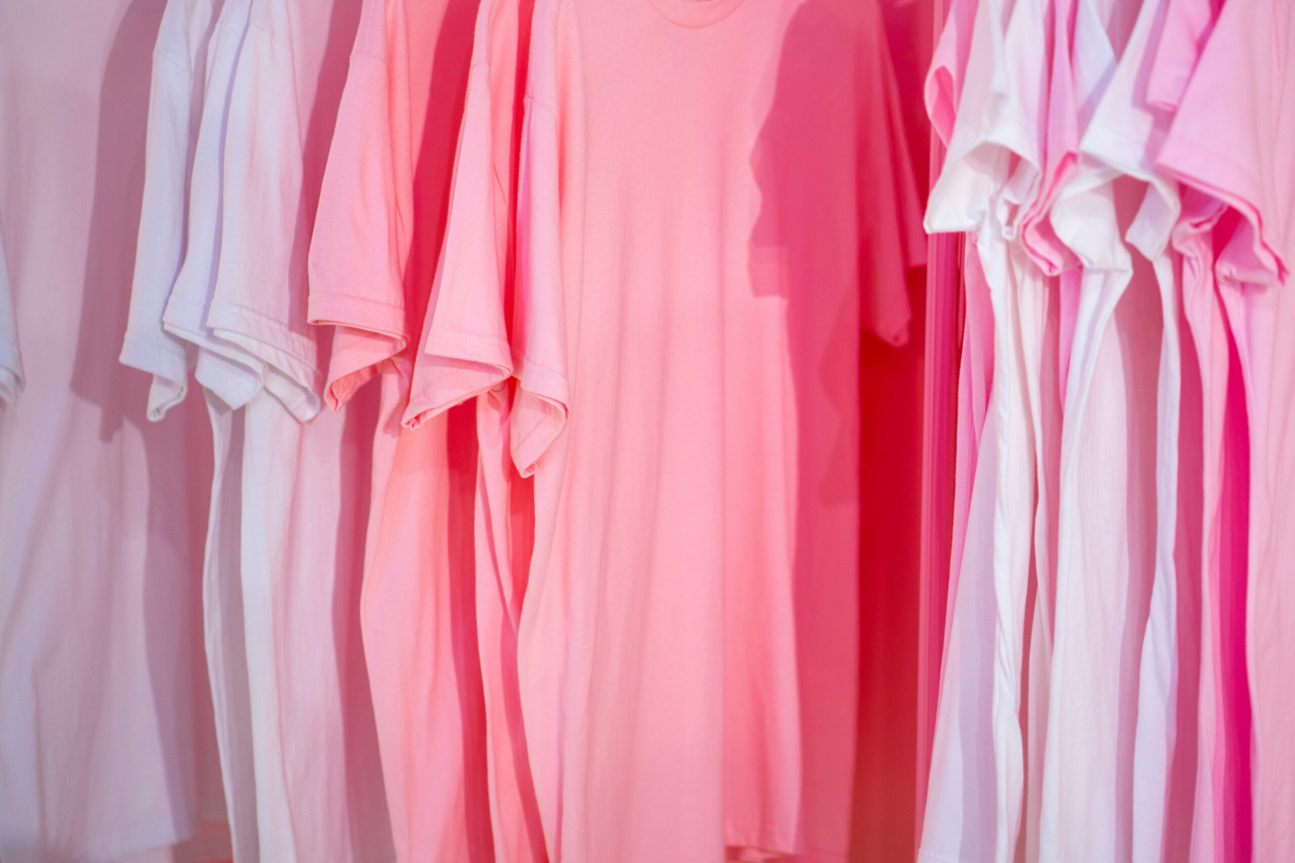 Several pink t-shirts hanging on a clothing rack.