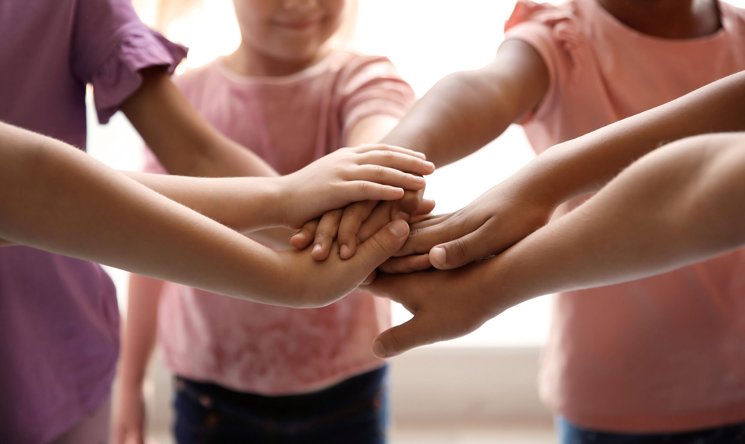 Young kids wearing pink shirts while holding their hands out in a pile.