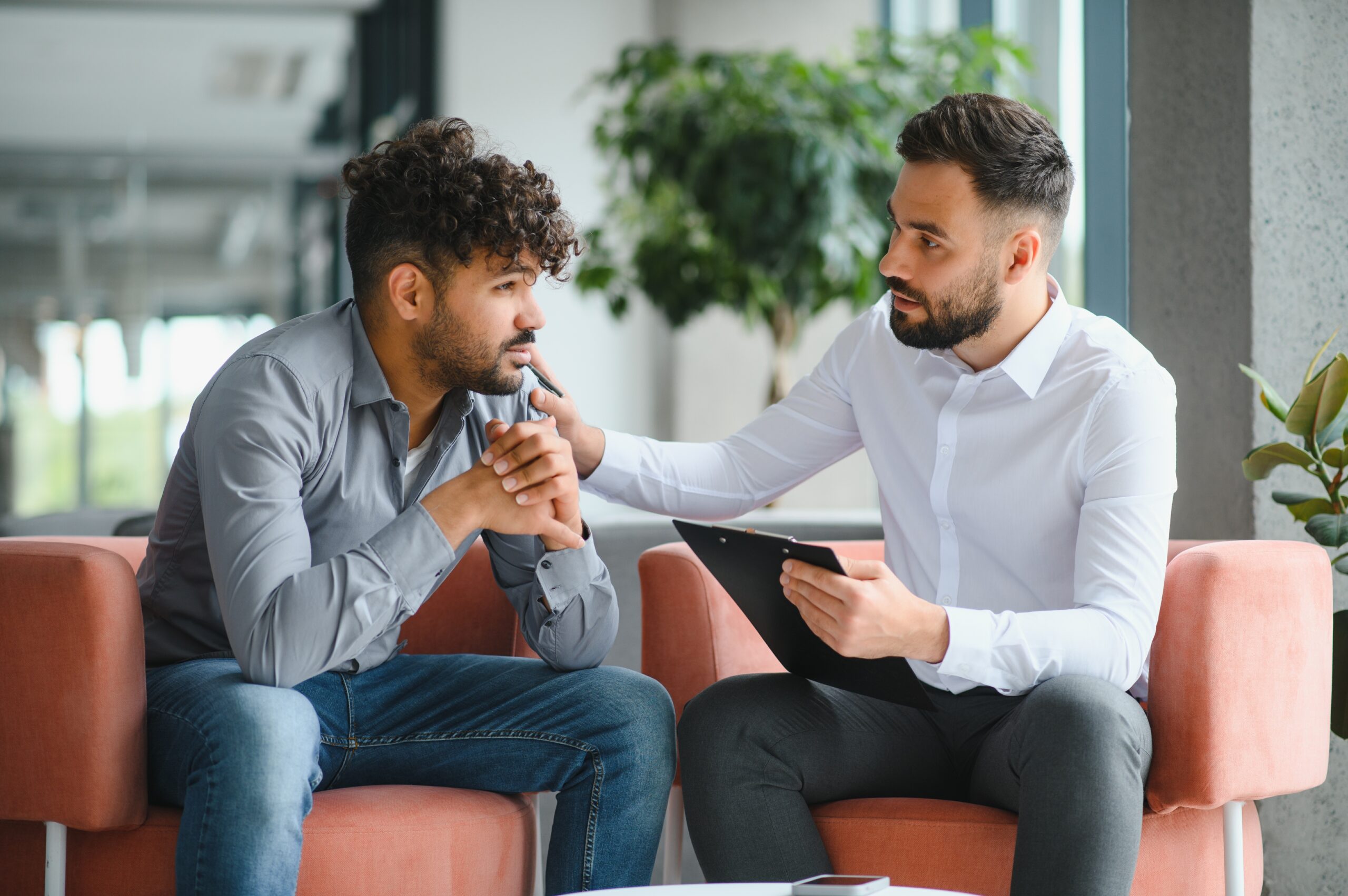 Two men sitting together. The man on the right has his hand on the other man's shoulder.