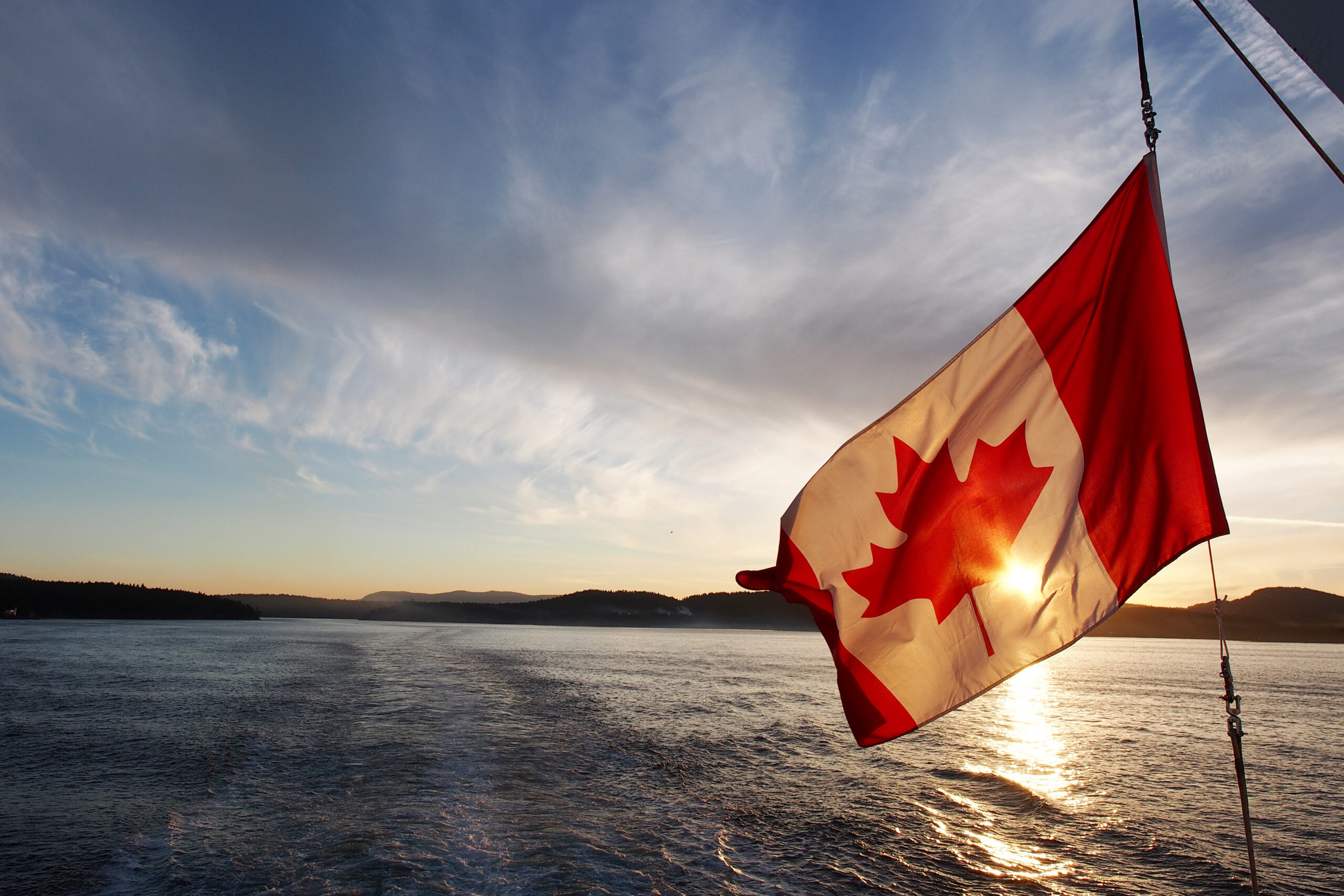 Canadian Flag blowing in the wind with a lake in the background.
