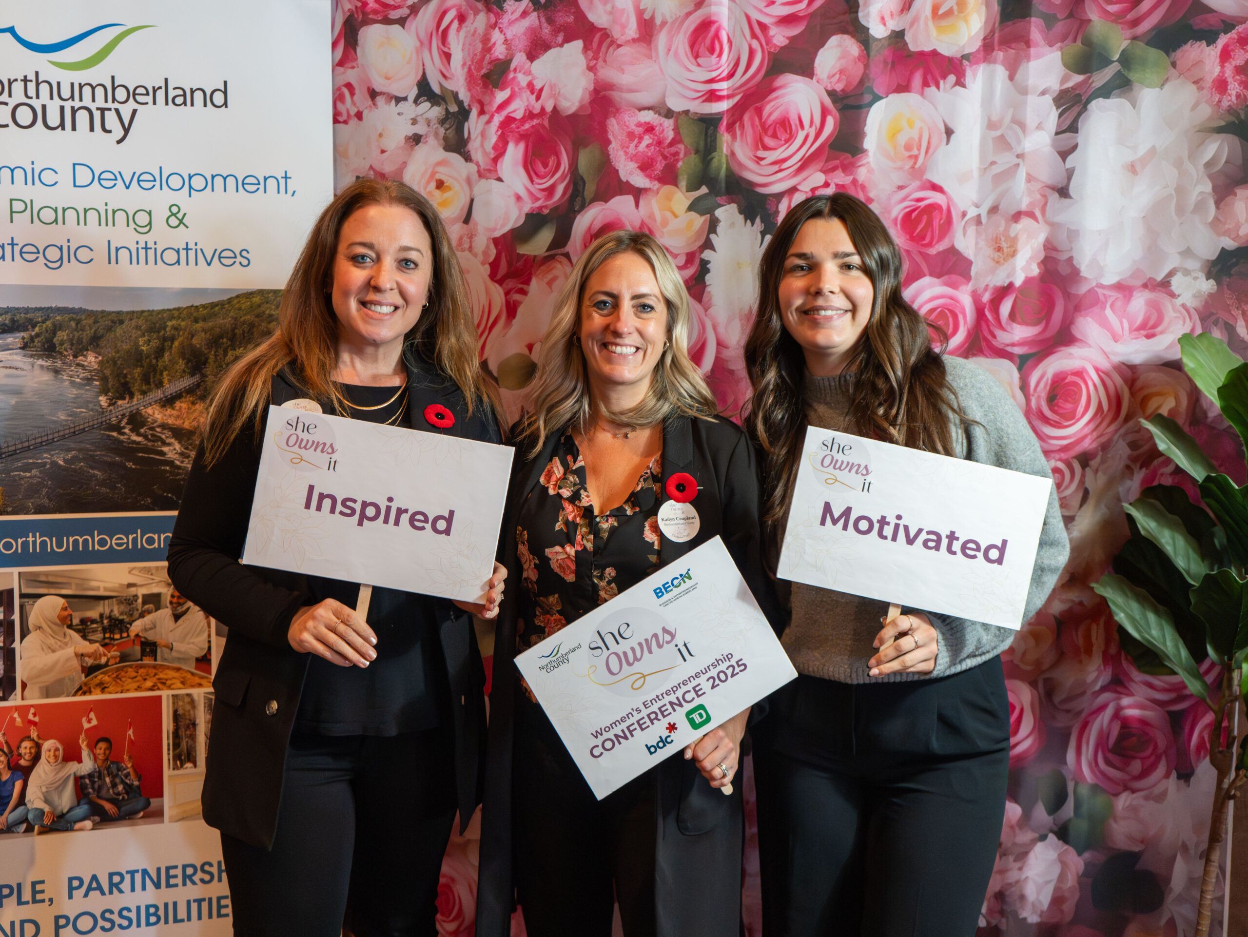 BECN staff pose in front of floral photo wall at She Owns It Conference
