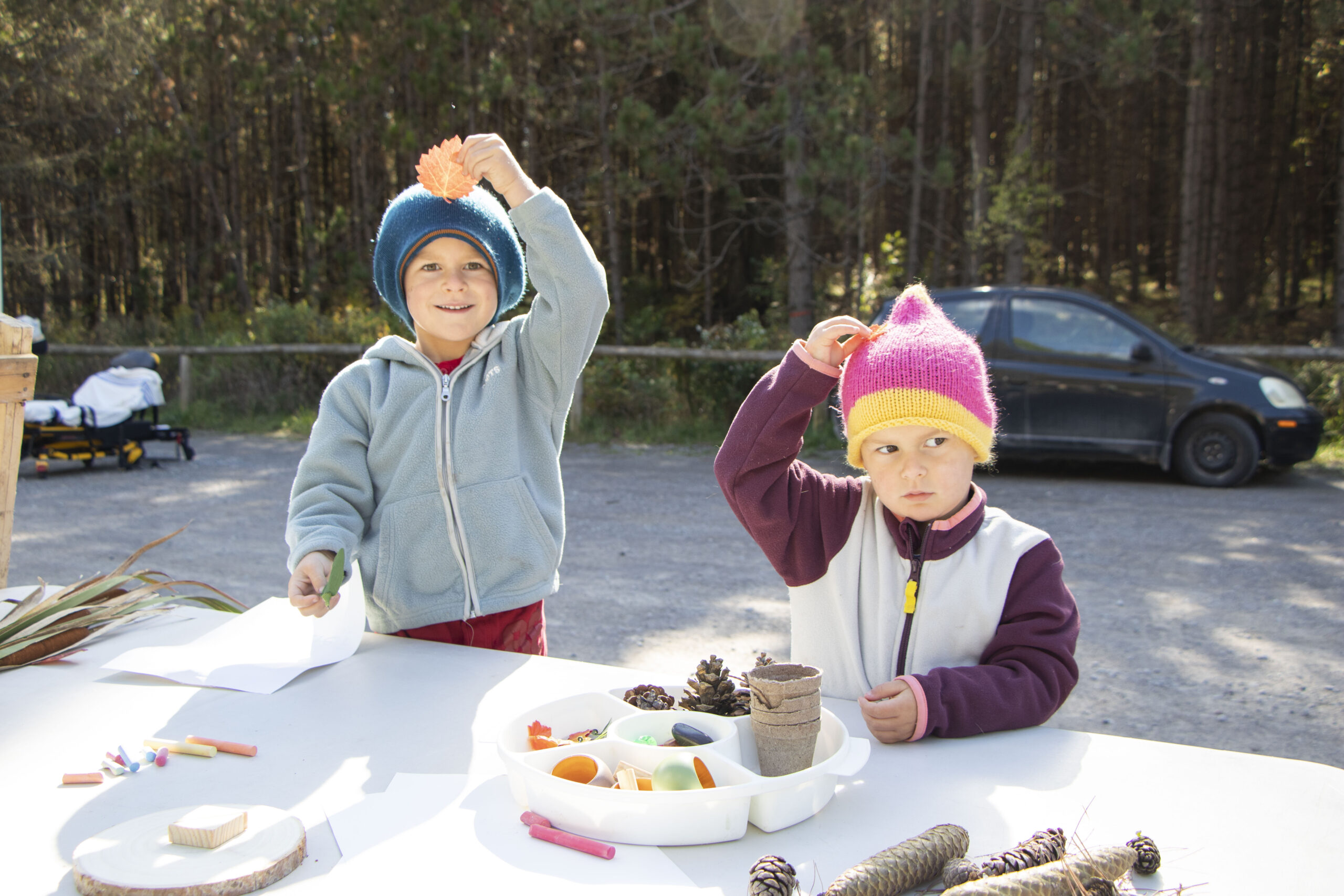 Two kids hold up leaves at learning table in the County forest