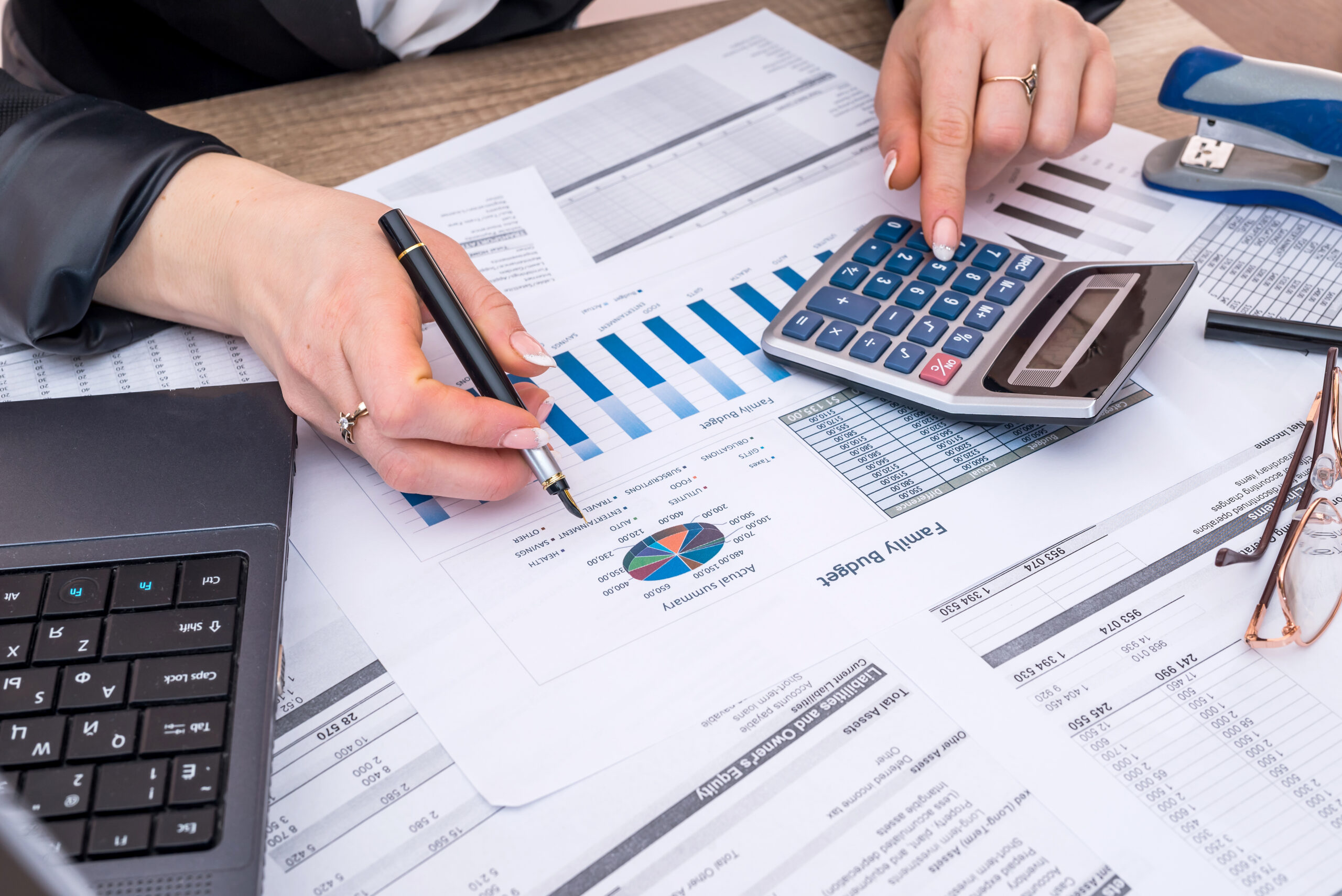 Staff member working on financial documents with one hand on a calculator.