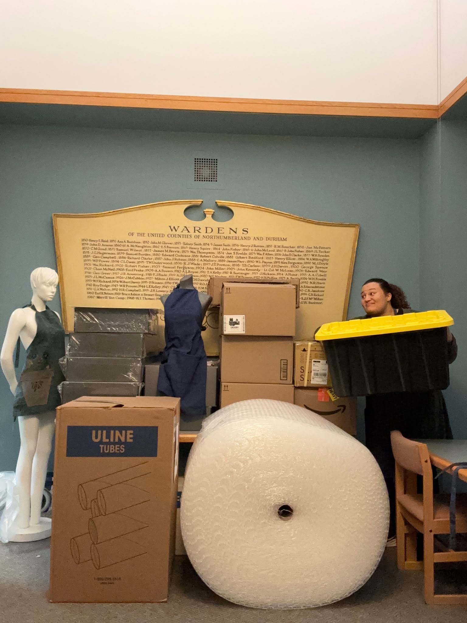 Museum staff carries box next to pile of moving boxes and supplies