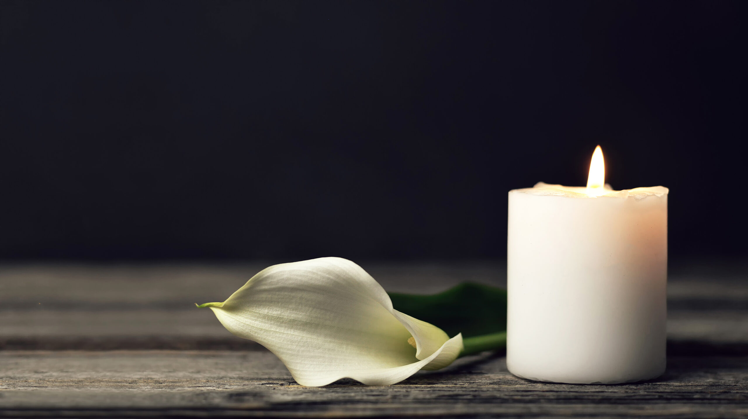 Solemn candle burning with a flower next to it.