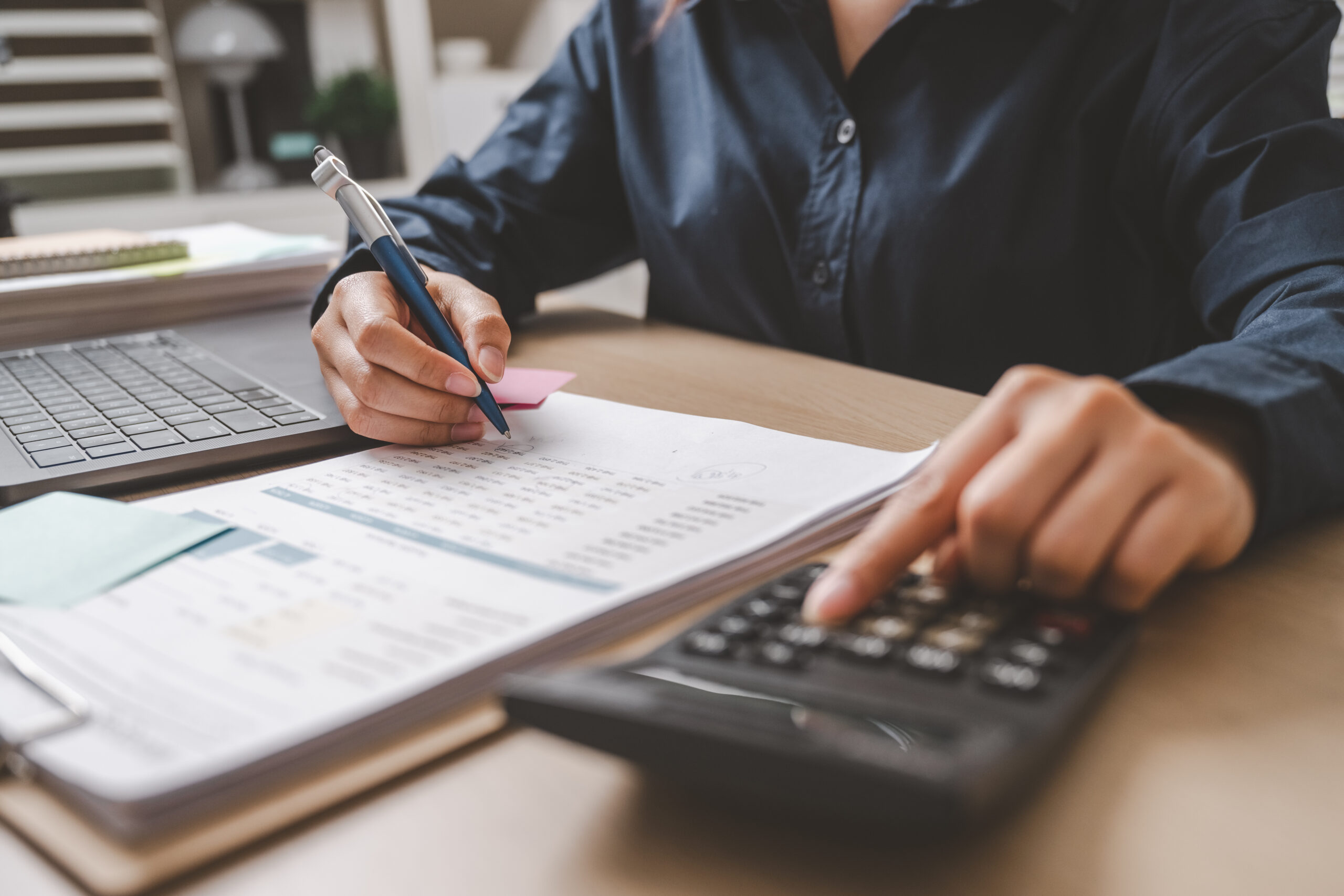Person holding a pen with one hand and the other hand typing on a calculator.