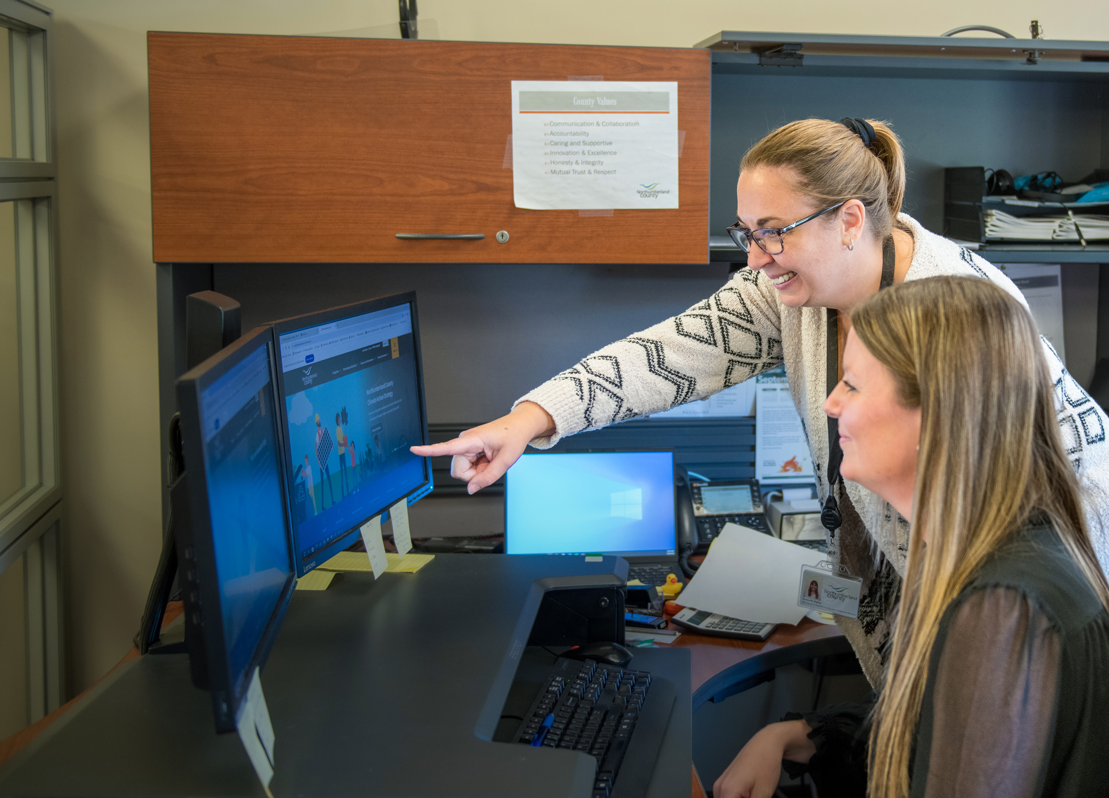 HR staff points over the shoulder of co-worker at computer screen