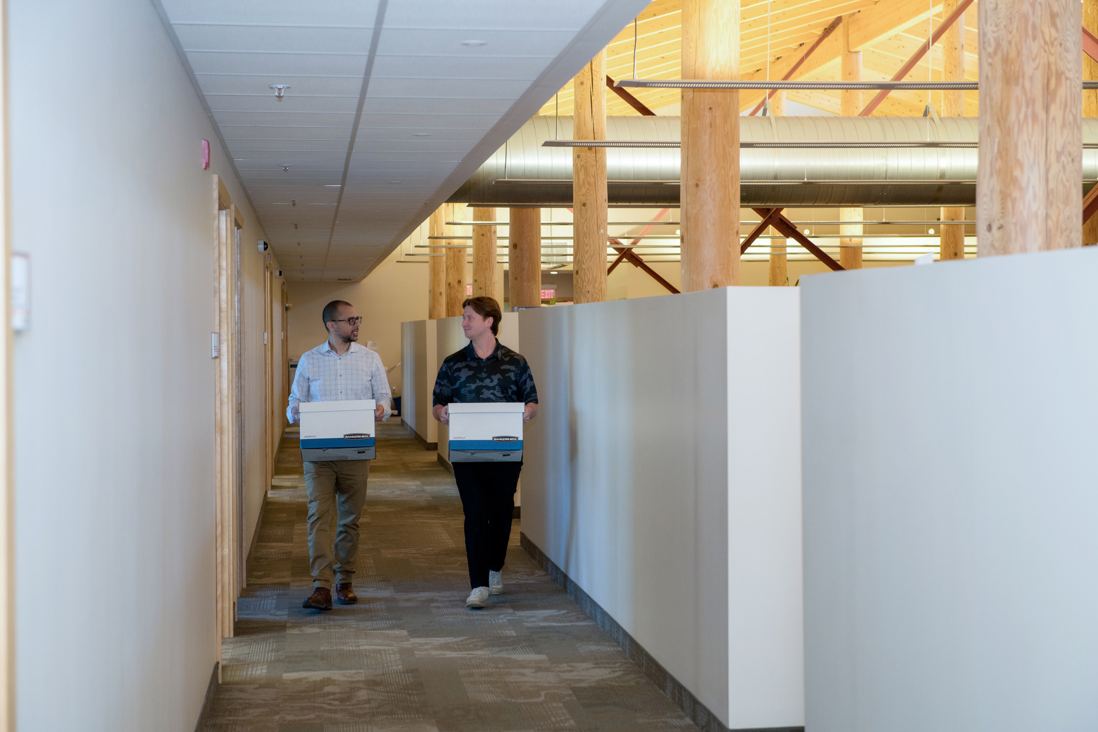 Two Finance staff members walk down the hall, carrying bankers boxes