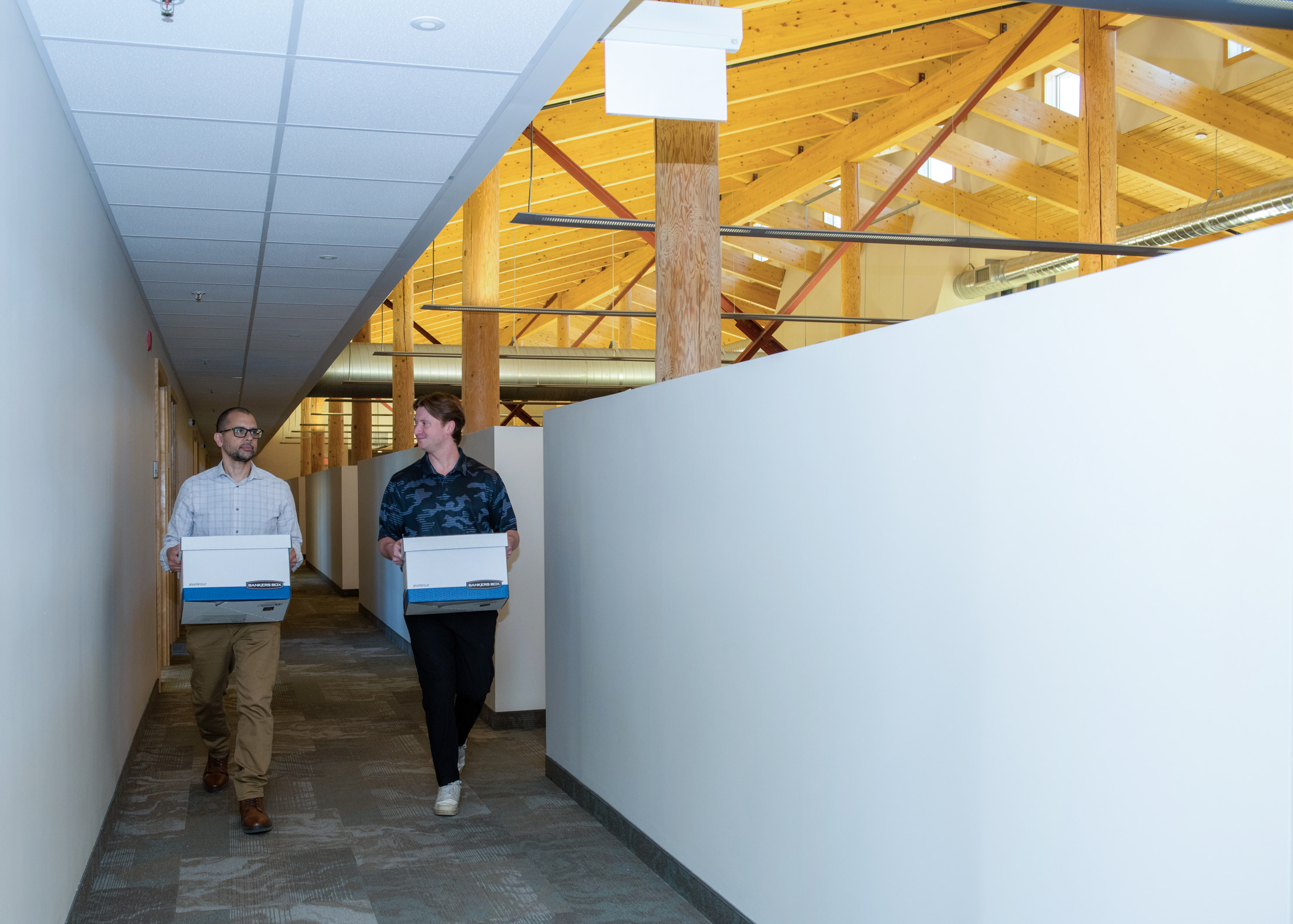 Two staff walk with bankers boxes down a hallway