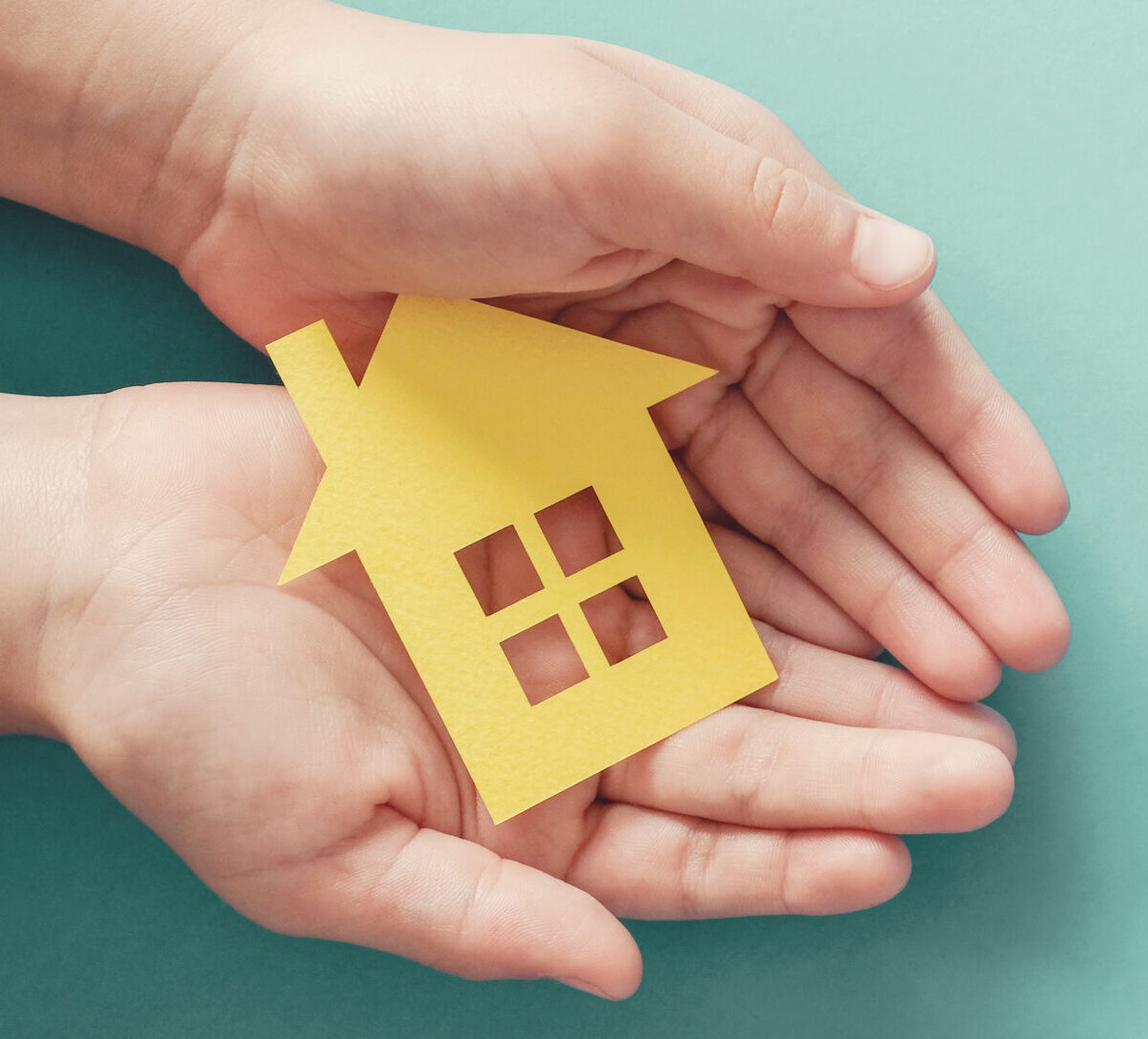 Hands holding a paper cutout of a house.