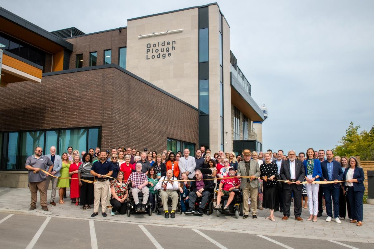 Group of attendees and residents standing in front of the new GPL cutting a gold ribbon.