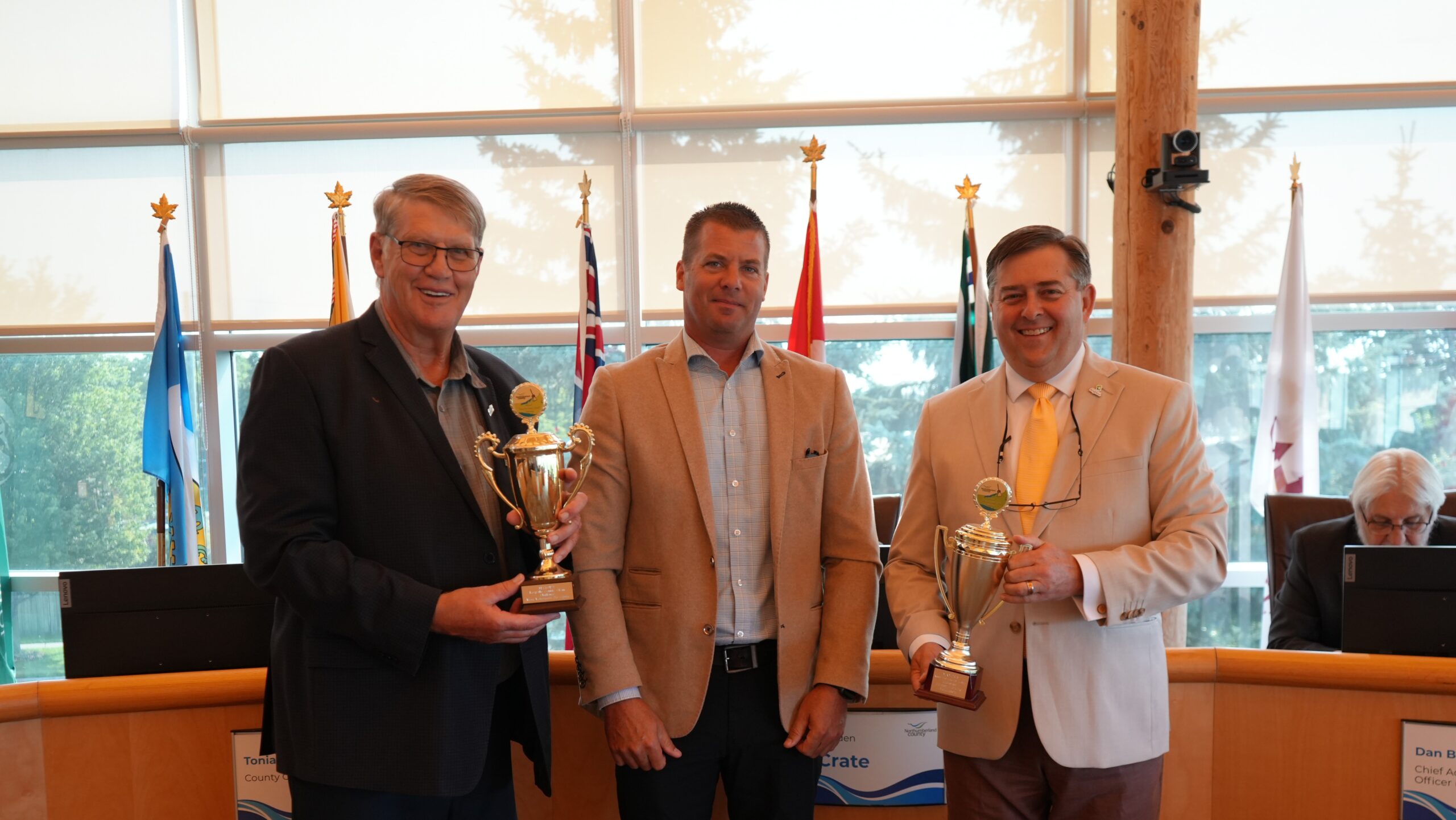 Councillor Ostrander and Councillor Logel standing with their trophies with a County staff member in Council Chambers.