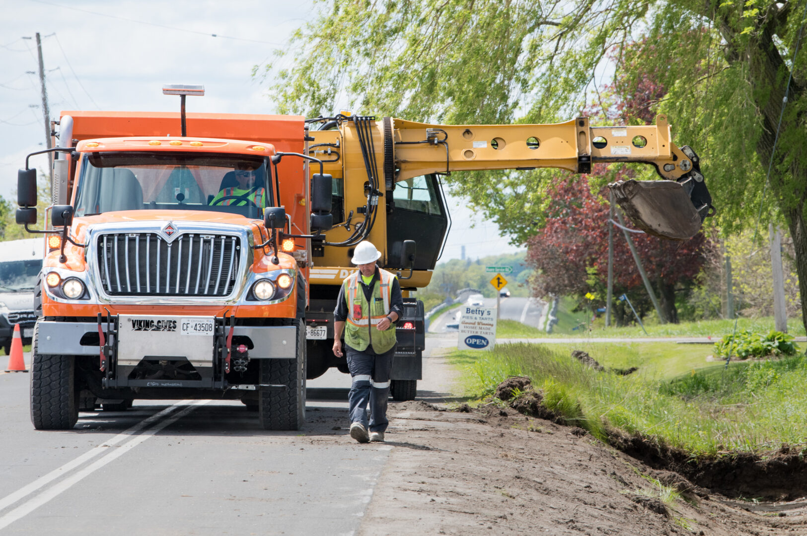Roads crew member walks beside ditch under construction, in front of construction truck