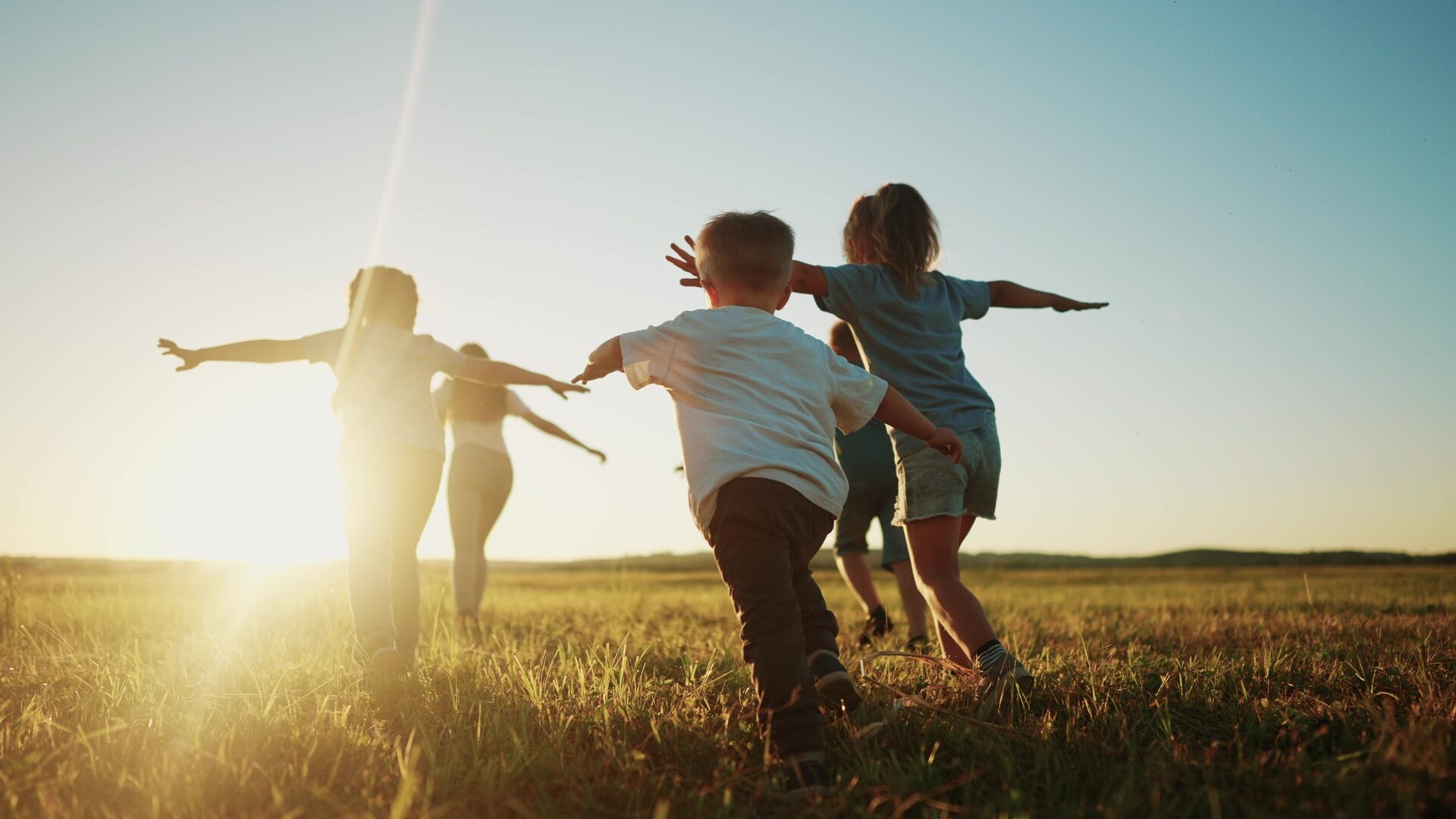 Four kids run in a field, towards a setting sun