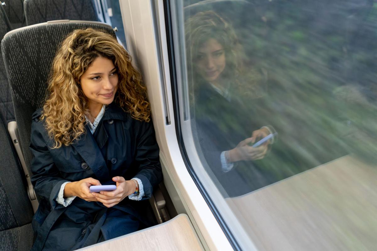 Woman on train looks out window while holding phone