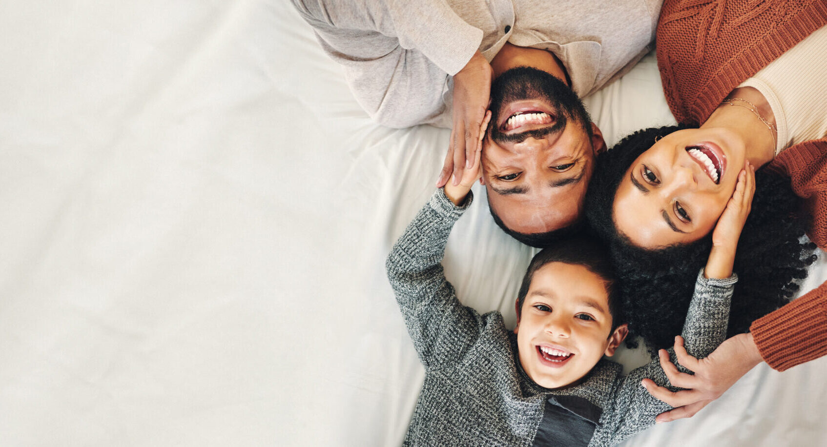 Top view, portrait of mom, dad and son smiling up at the camera while laying on the floor, heads together in a circle